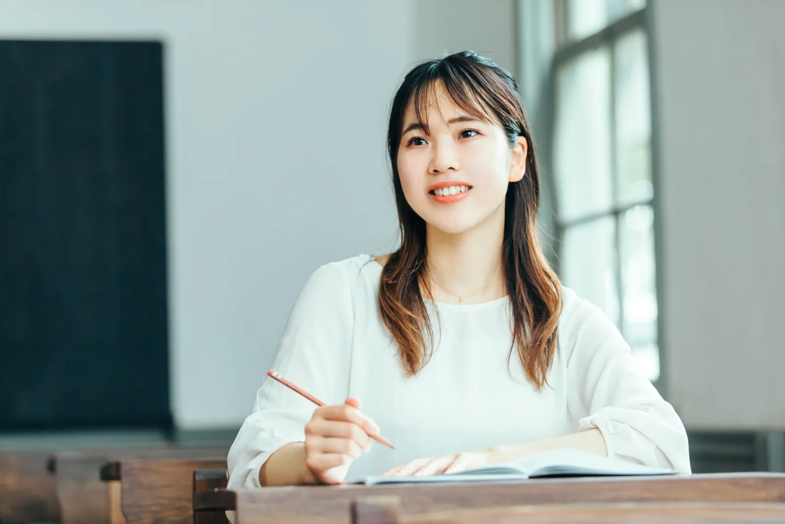 教室でノートを取りながら微笑む大学2年生のSさん