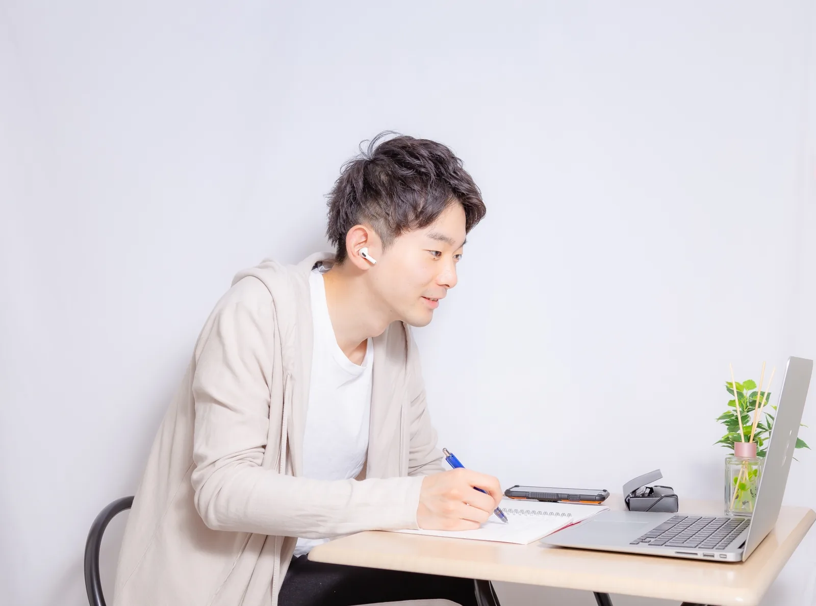 イヤホンでオンライン講義を受けながらノートを取る男性